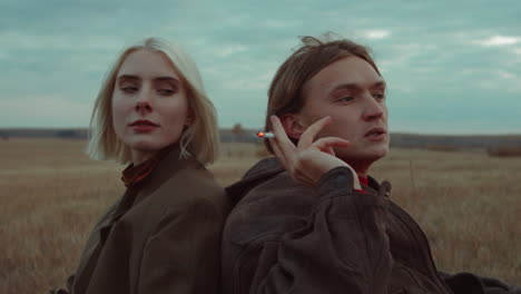 Couple-Sitting-on-Field-and-Smoking-Cigarette