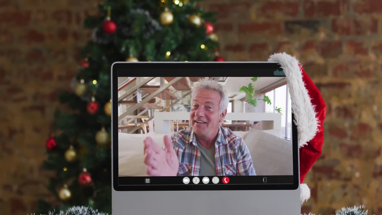 hombre caucásico de alto nivel saludando en una videollamada en la computadora, con decoraciones de navidad y árbol