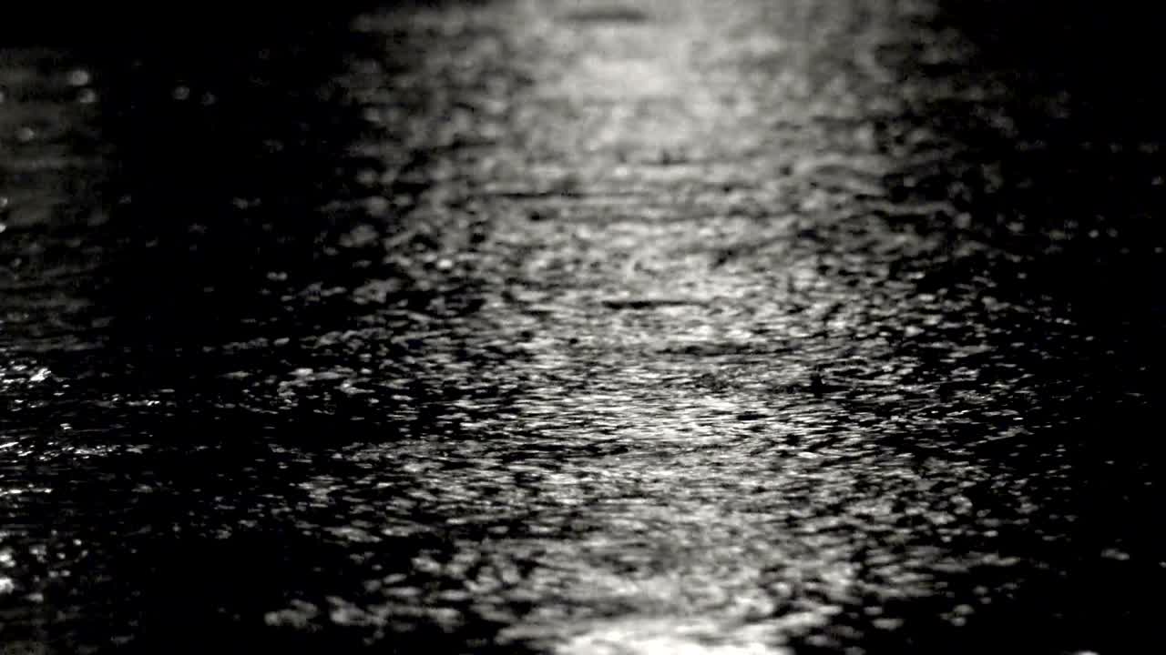 Closeup footage rain on water surface with reflection at dark night, loop background