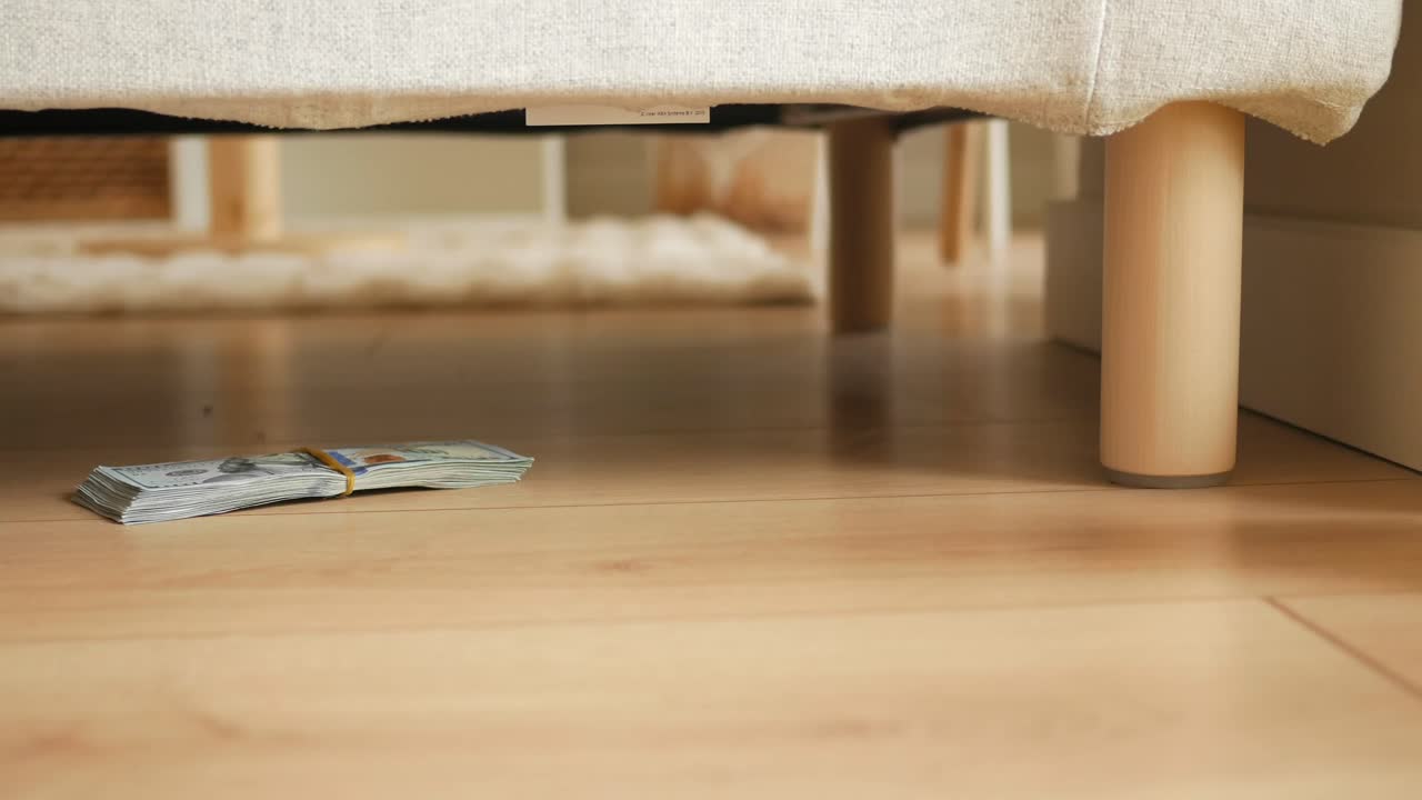A Stack of Money Hidden Under Furniture on a Wooden Floor