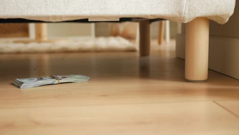 a stack of money hidden under furniture on a wooden floor