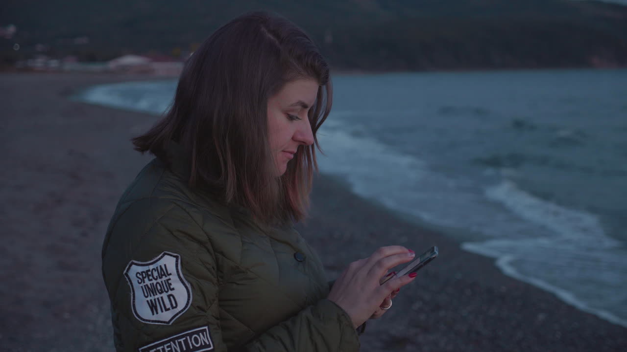 toma en cámara lenta de una chica usando su teléfono en la playa al atardecer