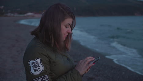 slow motion shot of a girl using her phone on the beach on the sunset