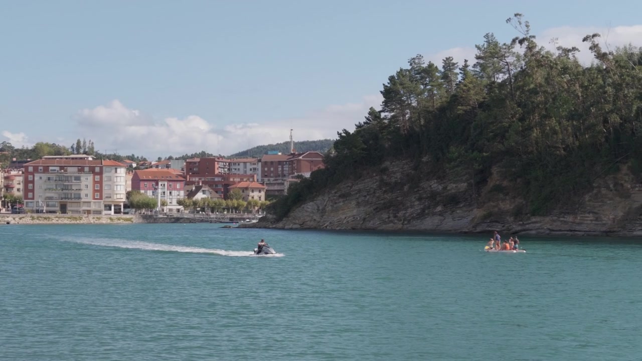Persone che praticano sport acquatici estivi nell'estuario di Plentzia, nei Paesi Baschi, con una città costiera e colline verdi sullo sfondo