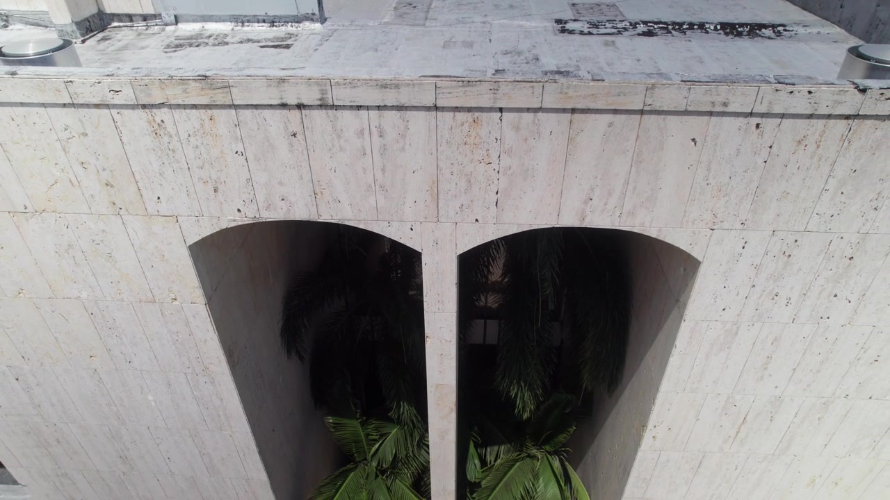 Ripresa verticale fluida del drone in tilt-up che cattura il dettaglio architettonico di un cortile interno, caratterizzato da pareti in marmo e palme curate presso il Teatro Nazionale, Repubblica Dominicana