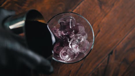 el camarero con guantes negros está vertiendo una bebida púrpura en un vaso lleno de cubos de hielo