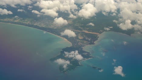 bird's-eye perspective from airplane window with view of clouds and tropical island with beaches