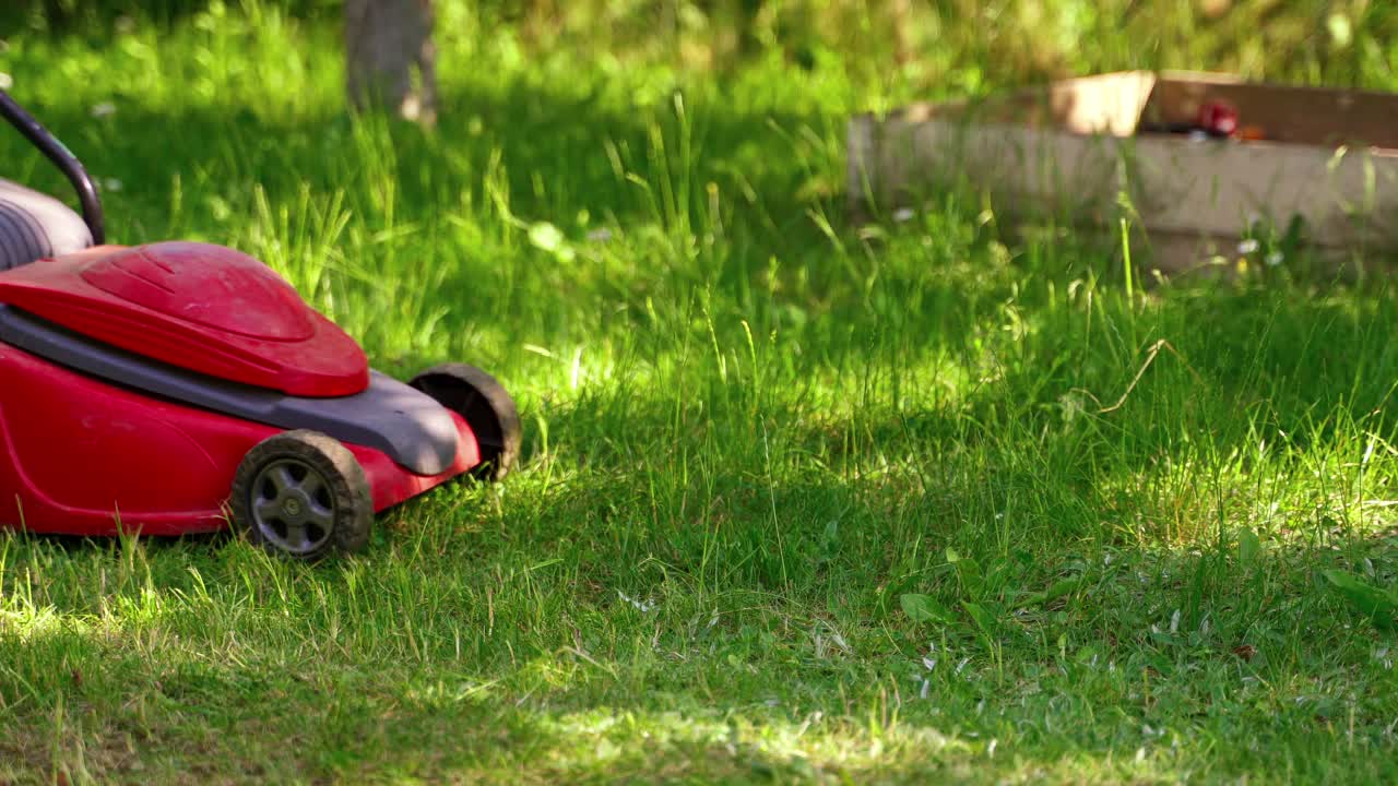 Mowing grass with lawn mower. Close up of mower cutting the grass