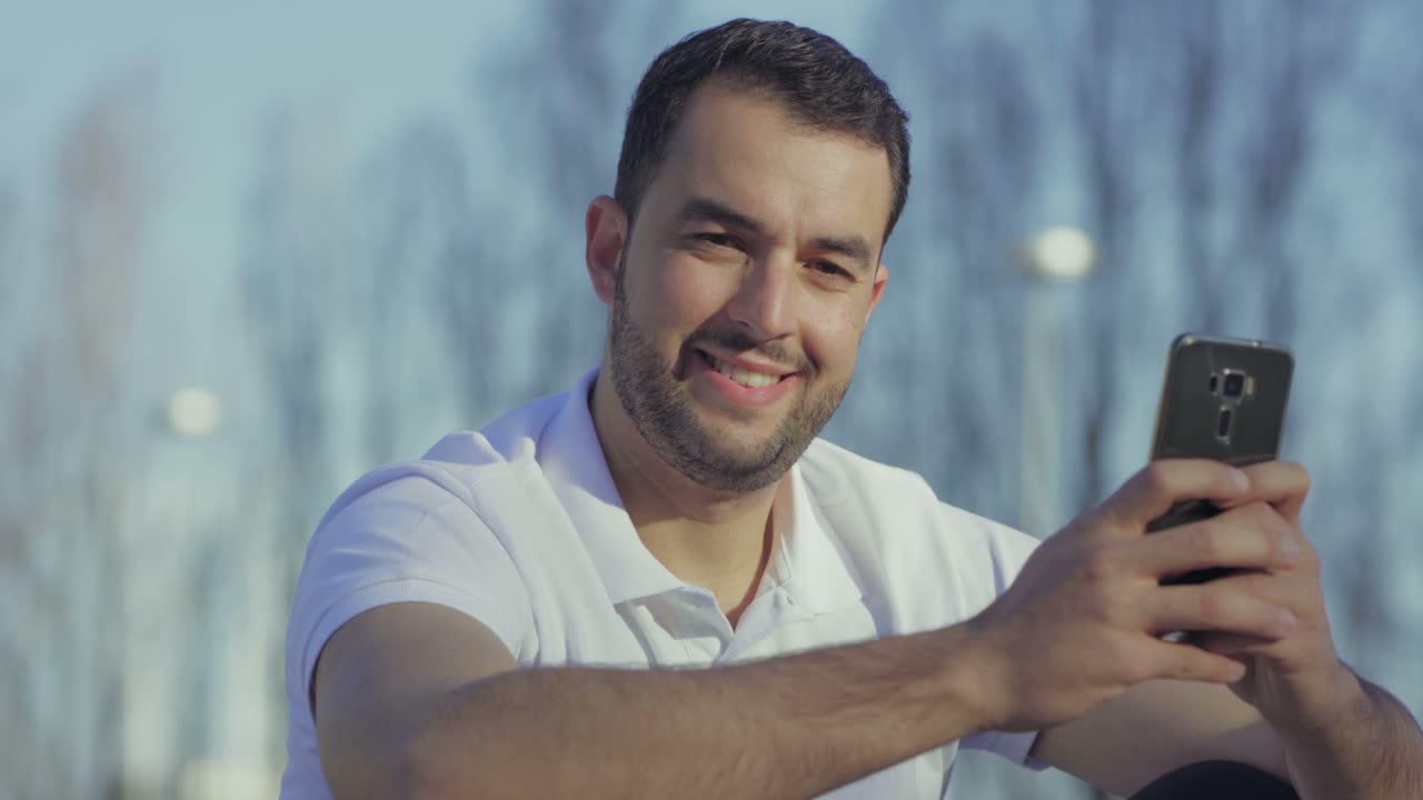 Homem barbudo sorrindo com smartphone em um dia ensolarado de verão.