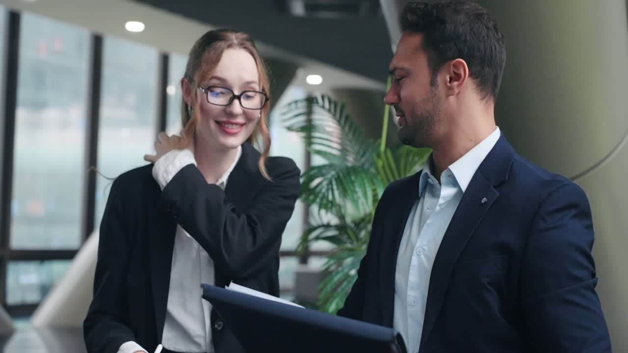Two Business Colleagues In Suits, Woman With A Tablet And A Man With A Folder, Happily Smiling And Laughing Together In The Office. - closeup shot