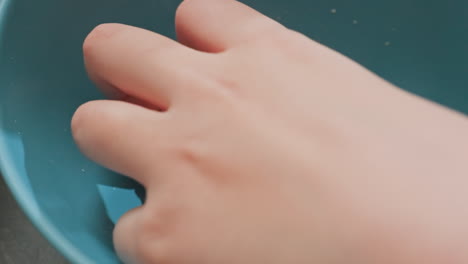close up hand view of fair skinned person packing caramel popcorn from blue bowl on dark table with candy in green bowl nearby, indoor casual snack moment with focus on fingers and texture