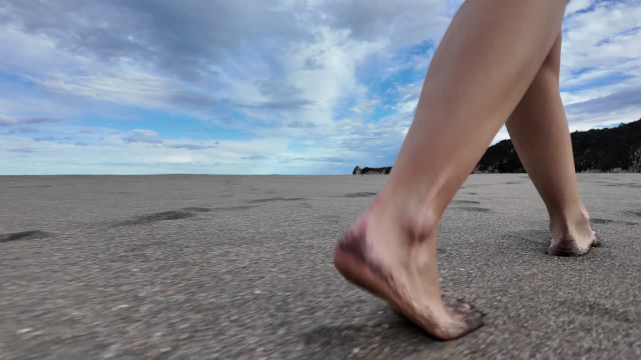 Slow-motion shot of a barefoot woman walking across an empty beach, symbolizing hope and moving forward