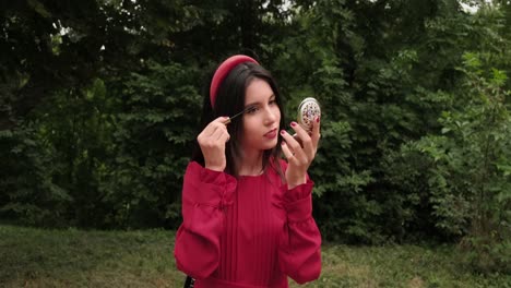 cheerful girl in red draws eyelashes in park