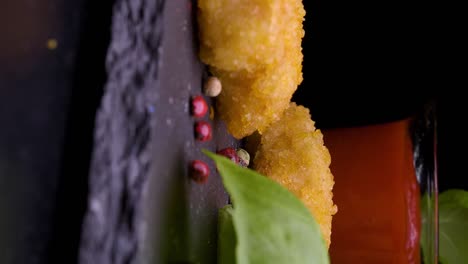 static vertical shot of vegan chicken nuggets spinning on slate with peppercorns, ketchup, and basi