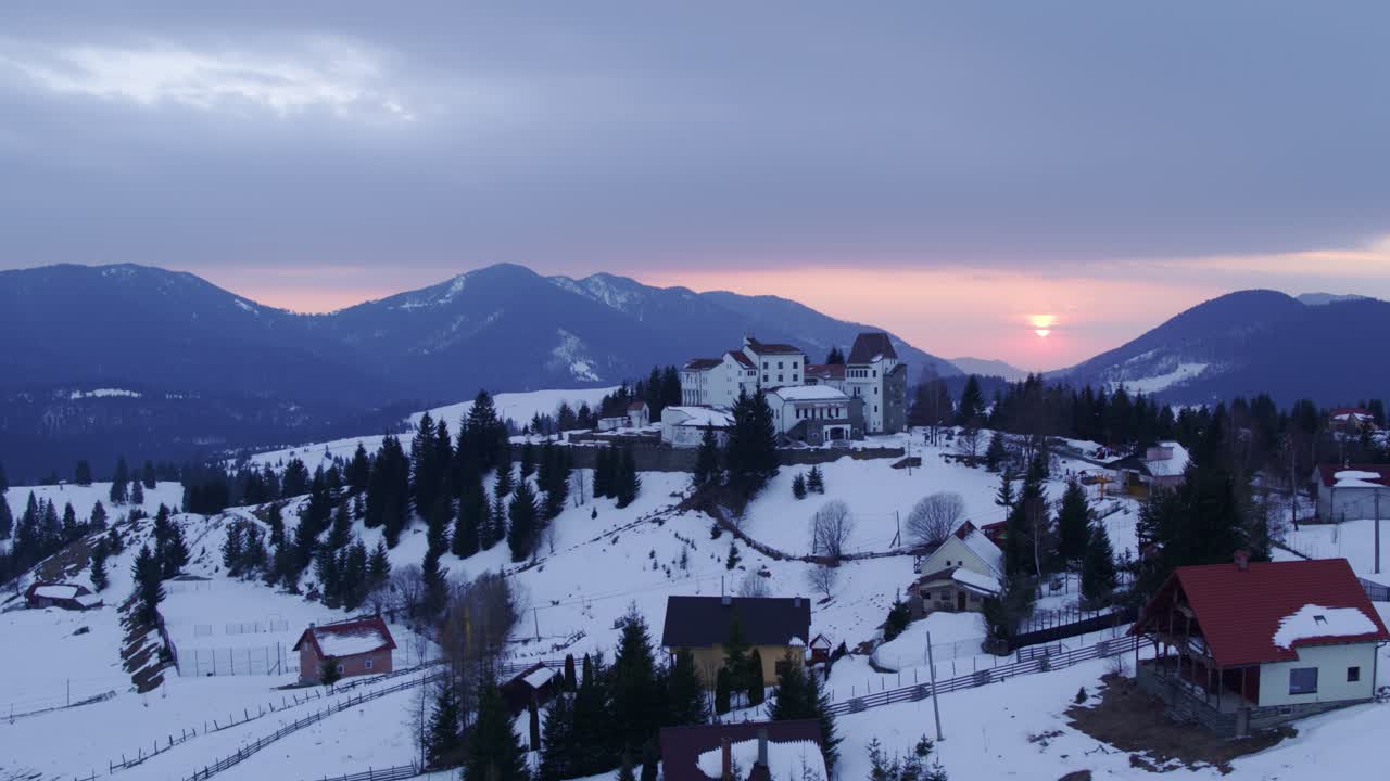 Aerial shot of a snowy mountain village with a castle during sunrise. Colibita, Romania