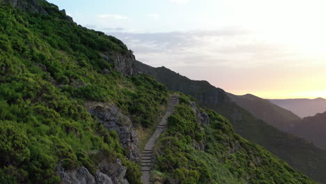 aerial view of hillside hiking trail in green mountains of madeira island with sunset horizon in background, portugal, drone shot