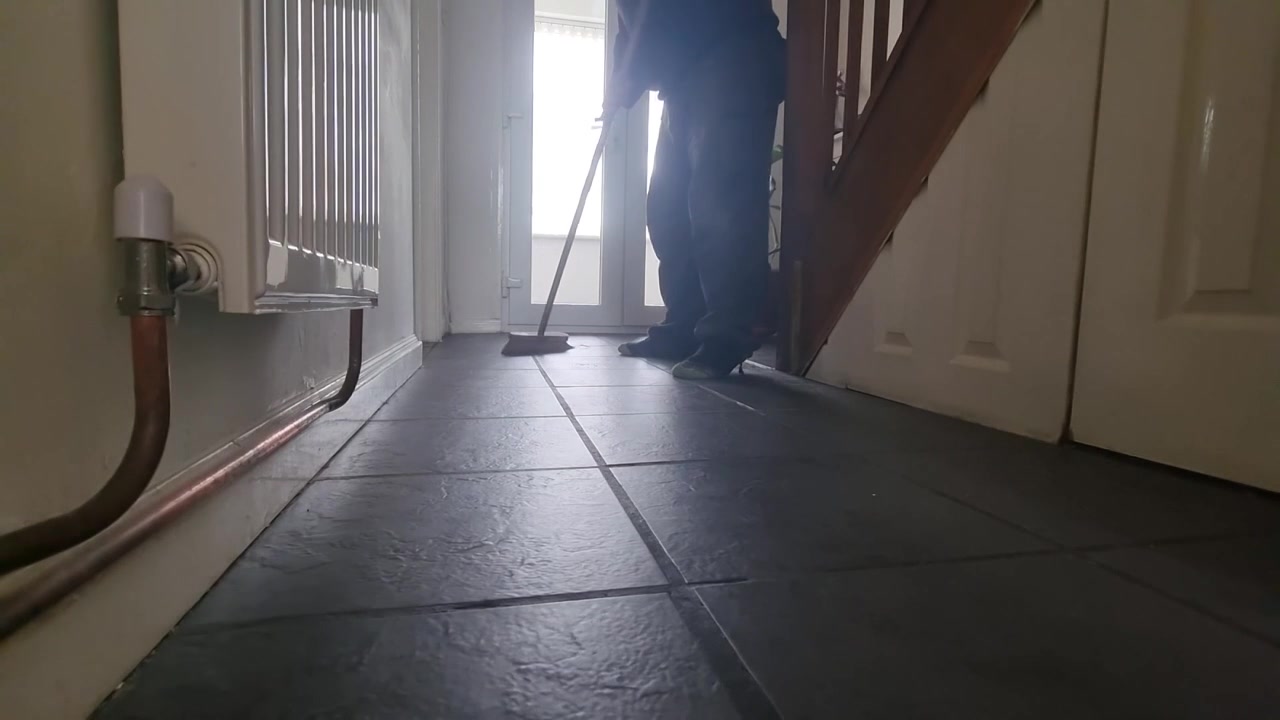 Low angle male wearing socks brushing hallway tiled flooring with household wooden brush closeup