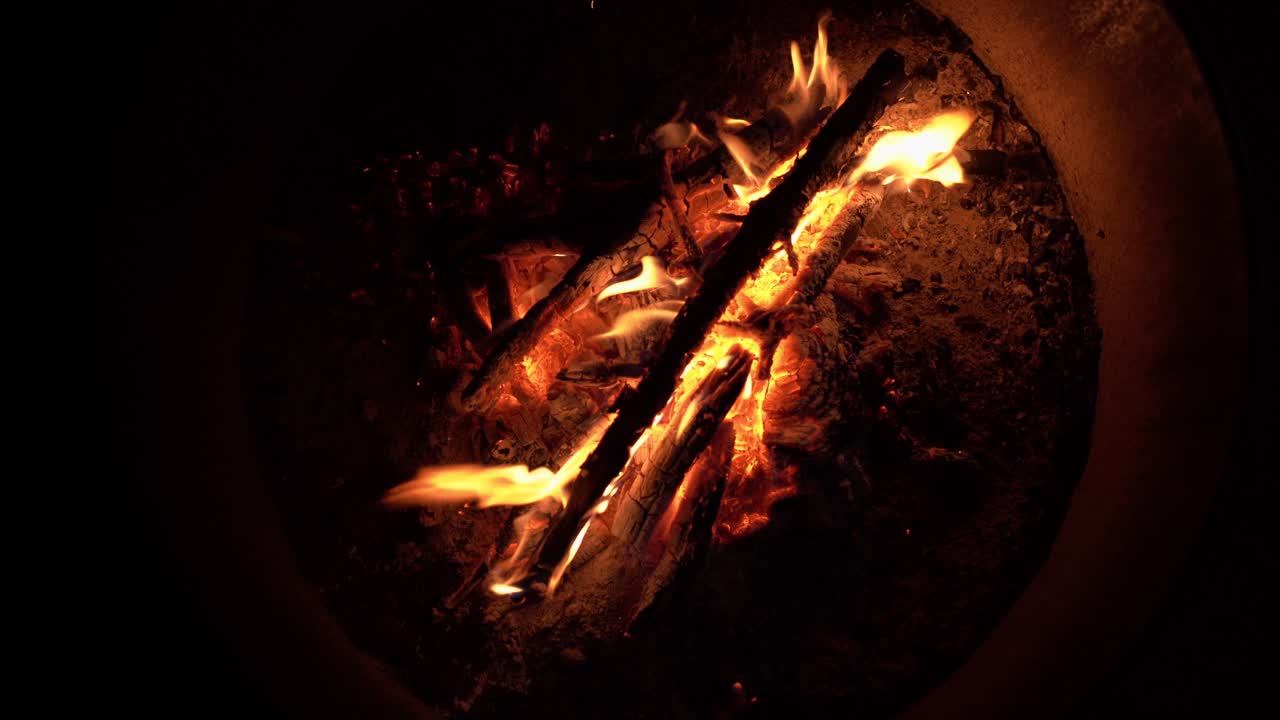 Close-up shot of flames burning on wood embers inside a fire ring at night, with the fire glowing in the dark