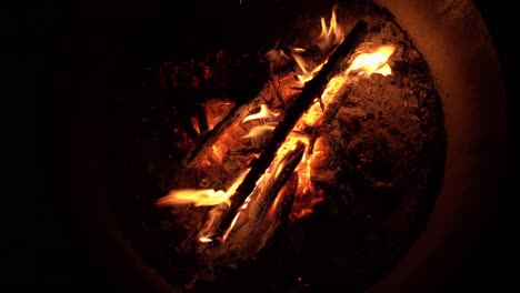 close-up shot of flames burning on wood embers inside a fire ring at night, with the fire glowing in the dark