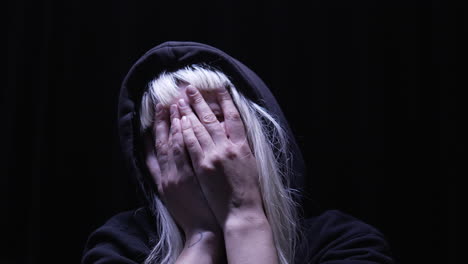 stressed person both hands on her face moving her head in disbelief in a dimly-lit room illuminated by a single overhead light