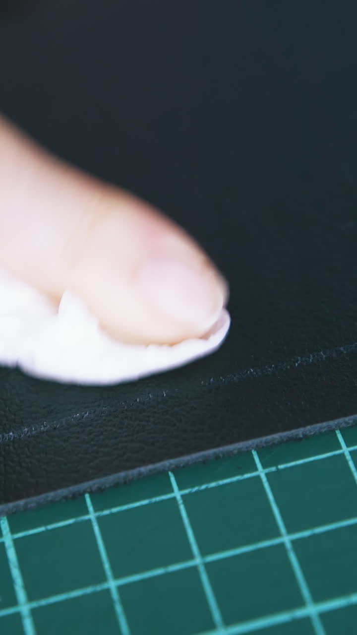 CU: Person hand wipes white line on black leather fabric with white paper napkin in workshop extreme close view