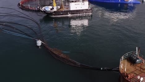 tilting drone shot of fish farming ships docked at an ocean fish cage