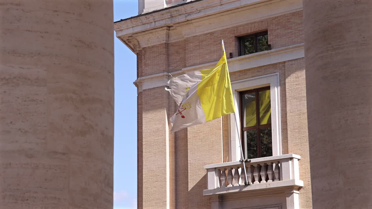 The yellow and white Vatican City flag flutters outside a historic brick building on a clear sunny day.
