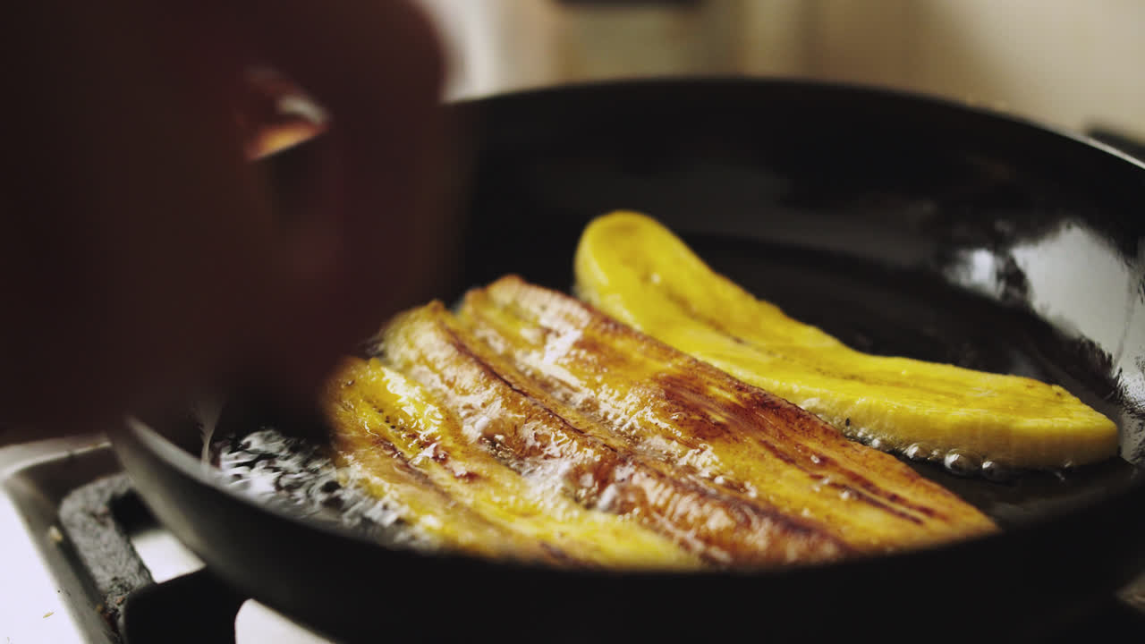 plano detalle de plátano ó banana friéndose en sartén negra con aceite
