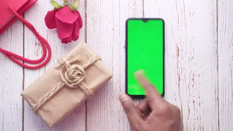 persona sosteniendo un regalo al lado de un teléfono con una pantalla verde