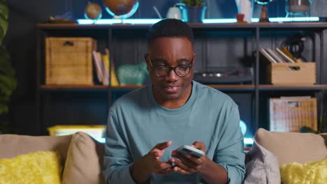 portrait of happy excited african male blogger nodding head to music shopping online using smart phone app at cozy home.