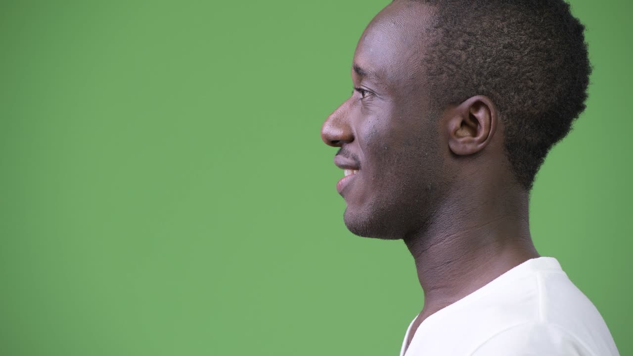 Profile view of young happy African man against green background