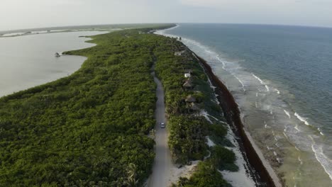 Aerial-view-of-a-white-car-on-a-beautiful-street-next-to-the-beach,-Mexico-4k