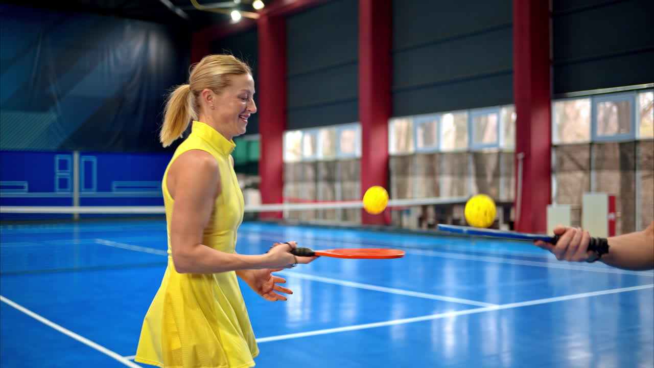 A man and a woman training to play pickleball on a blue, inside court