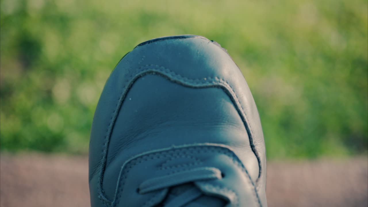 Close-up view of the tip of a white shoe on a grassy and blurred background