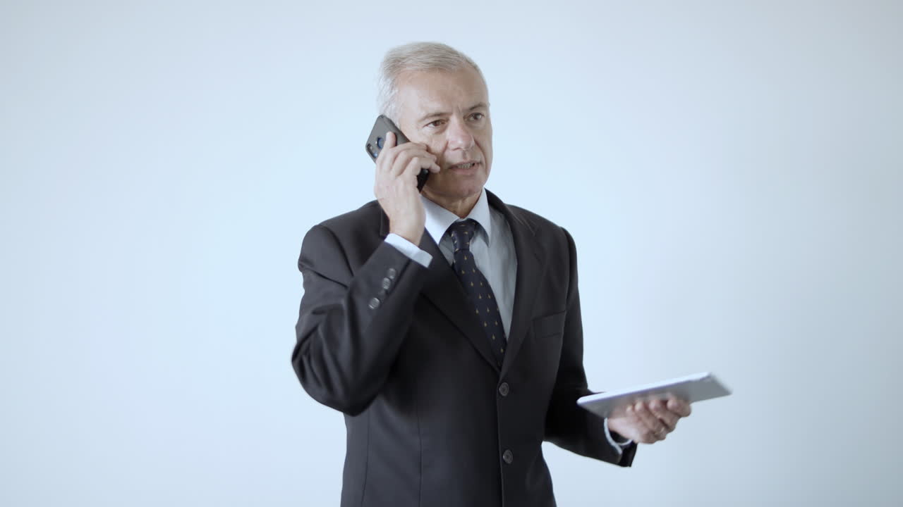 양복과 넥타이 태블릿을 들고 전화 통화에 심각한 회색 머리 사업가