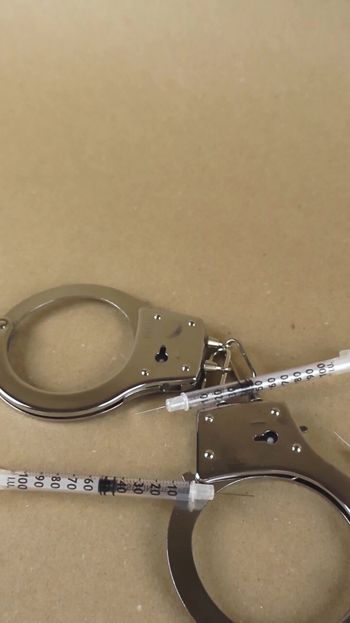 Manette metalliche e siringhe multiple appoggiate su uno sfondo neutro, che rappresentano le conseguenze penali della tossicodipendenza, dell'abuso di sostanze, del traffico e del possesso illegale