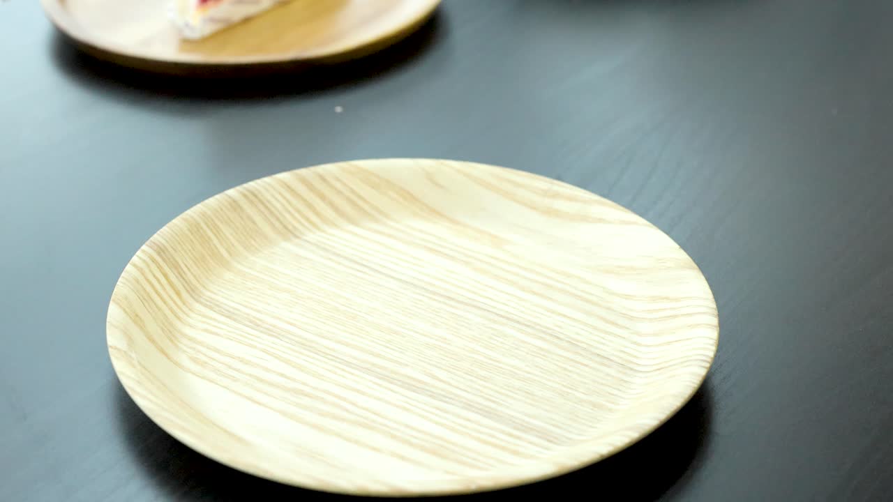 Hand places chocolate cake slice with strawberry topping onto round wooden plate, bright natural lighting