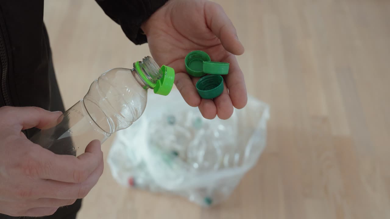 Primo piano di mani che rimuovono tappi di plastica verdi da una bottiglia in PET sopra un sacco per la raccolta differenziata, evidenziando la corretta separazione dei rifiuti e pratiche di riciclo responsabili a casa.