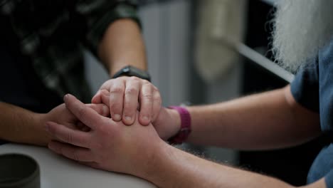 close up elderly and middle-aged men hold hands during their difficult conversation about relationships and relationships in lgbt couples of two men in the kitchen at the table during the day