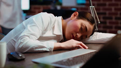 tired employee sleeping on workspace desk, awaken by coworker, laughing