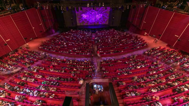 Spettatori si radunano nell'auditorium e guardano lo spettacolo a teatro, timelapse. Grande sala con poltrone rosse. Spettatori che riempiono i posti fino allo spegnimento delle luci. Vista dall'alto.