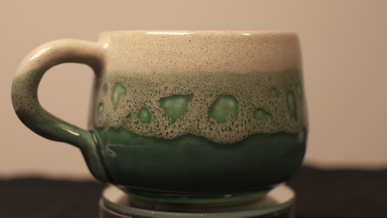 taza verde de cerámica casera exhibida en una plataforma giratoria