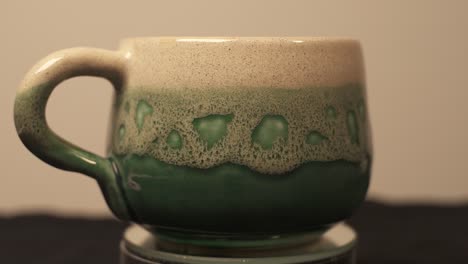 taza verde de cerámica casera exhibida en una plataforma giratoria