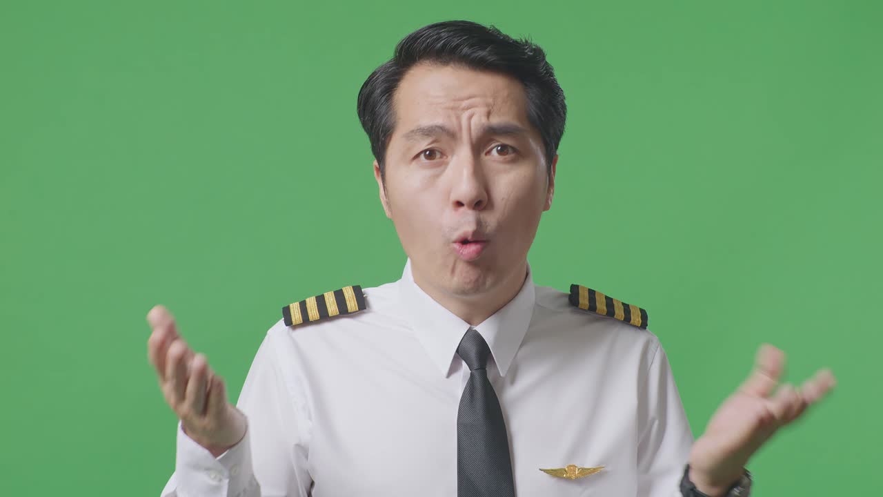 "아시안 남자 조종사가 ""왜?""라고 묻고 녹색 스크린 배경 스튜디오에서 의심스럽게 서 있습니다."
