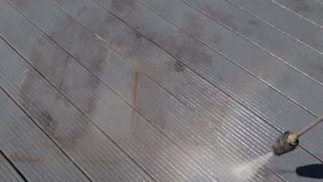 high pressure water jet cleaner washing dirty black deck outside and making a rainbow with the vapor