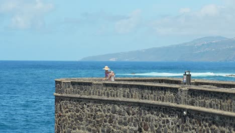 mother with baby on arm looks into the ocean breakwater, tenerife