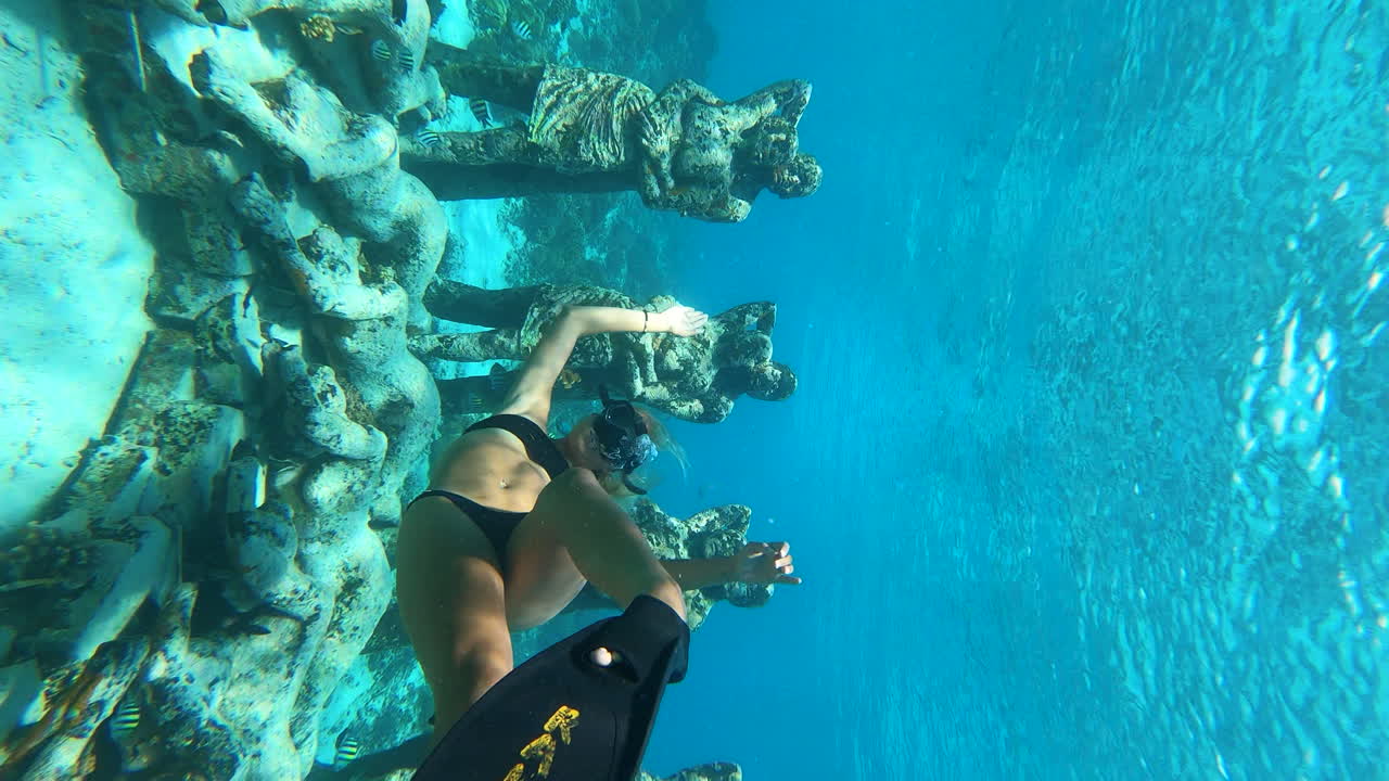 Beautiful female diver swimming underwater between the sculptures of Gili Meno statues, Gili Islands