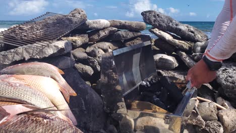 El-Hombre-Usa-Acero-Para-Encender-Fuego-Para-Encender-Una-Parrilla-De-Carbón,-Barbacoa-De-Pescado-Fresco-En-La-Playa-Caribeña