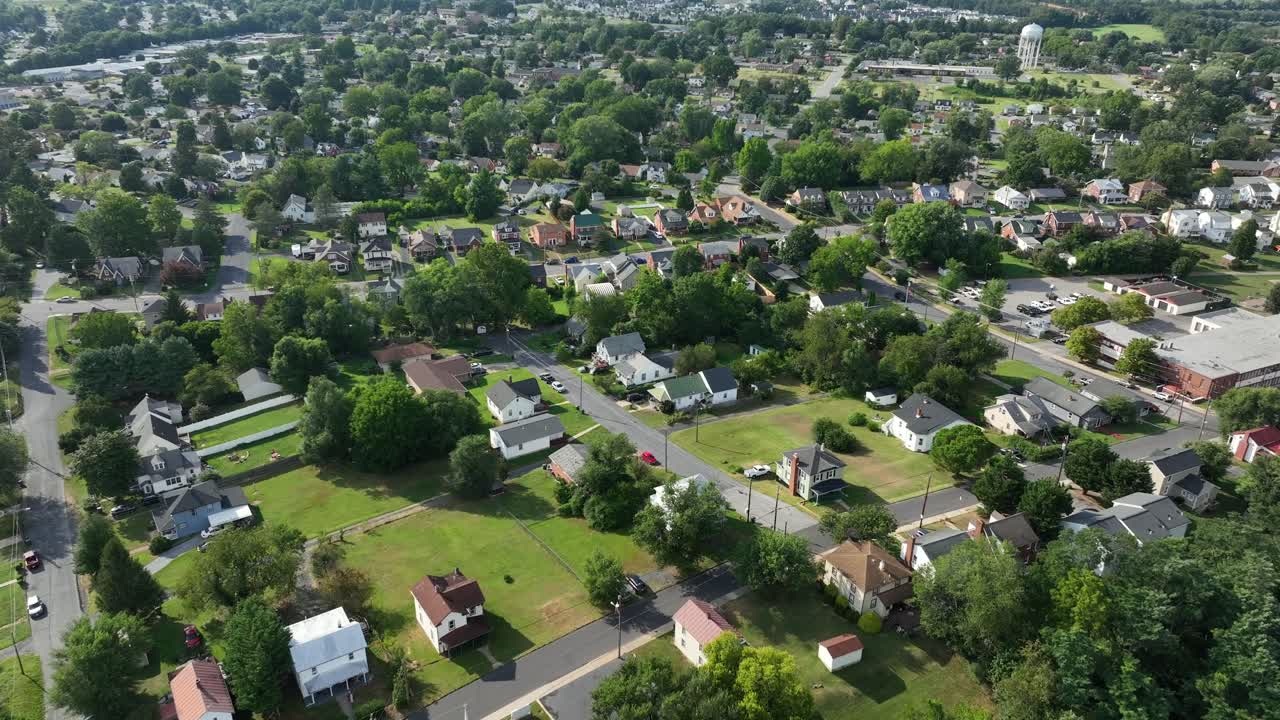 American neighborhood with green grass in garden at sunny day. Aerial flyover shot. Small suburb town and water tower in background. Virginia state of USA. Peaceful and serene atmosphere