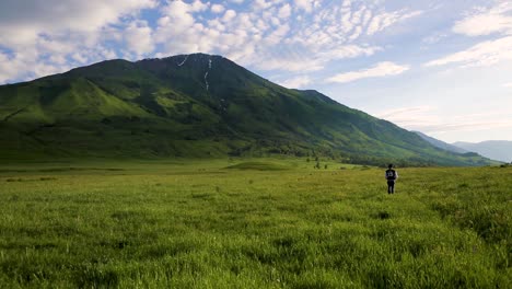 single person hiking in lush green mountainous meadow on a beautiful summers day, static shot